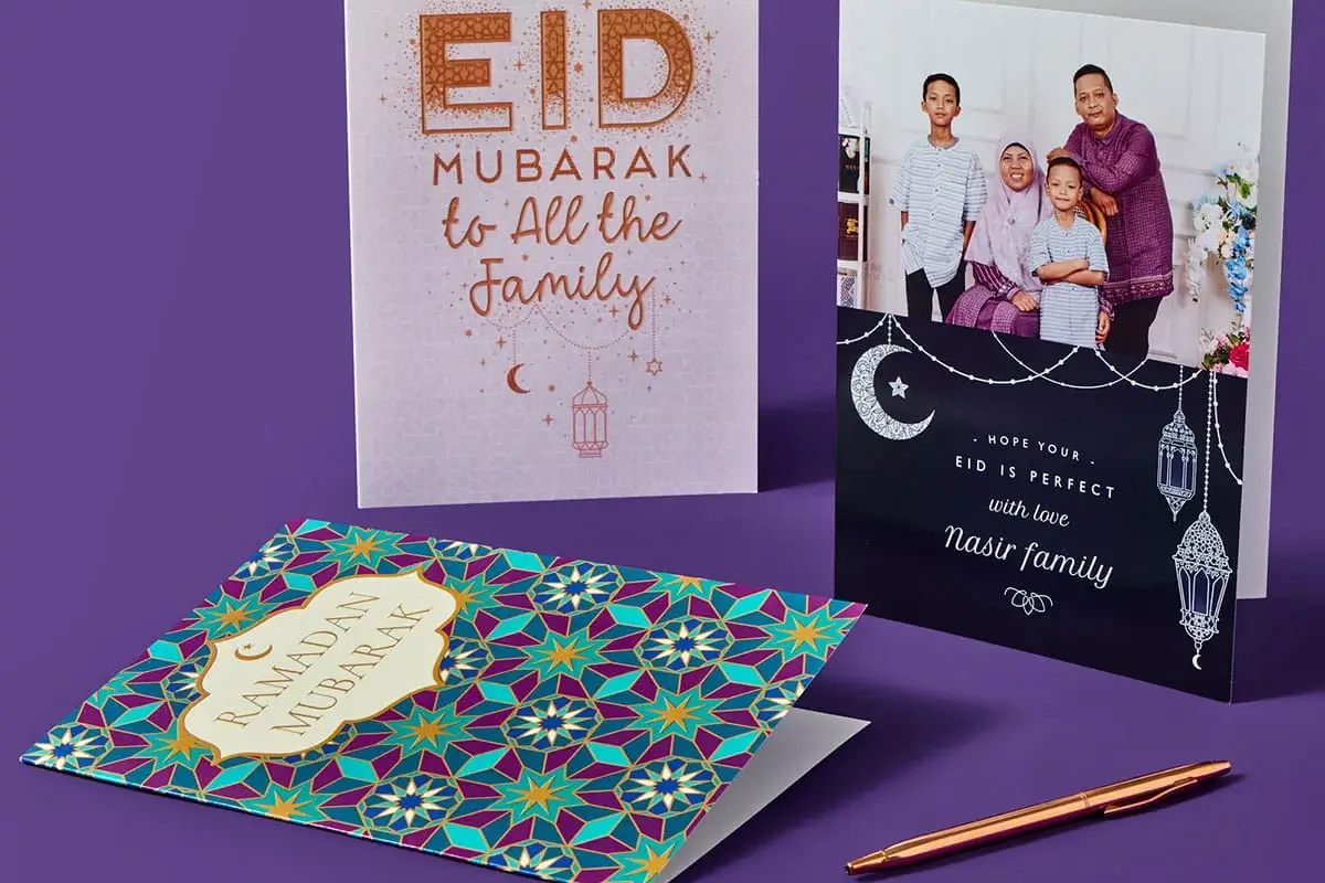 Three Eid and Ramadan greeting cards displayed on a purple surface, including a patterned Ramadan Mubarak card, a glittery Eid Mubarak card, and a personalised card featuring a family photo.